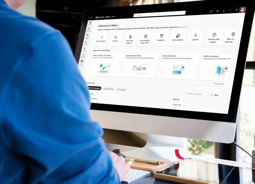 Person using a desktop computer showing the Microsoft Fabric home screen with quick-start tiles for new workspace, data engineering, lakehouse, and warehouse.